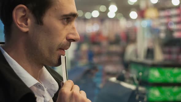 A Young Man with a Credit Card Hesitate in Buying at the Storefront