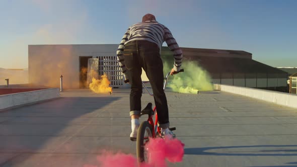 BMX rider on a rooftop jumping and using smoke grenades