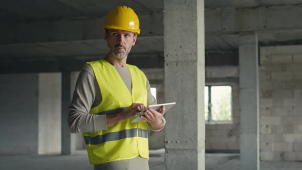 Caucasian engineer walking and browsing digital tablet on construction site.