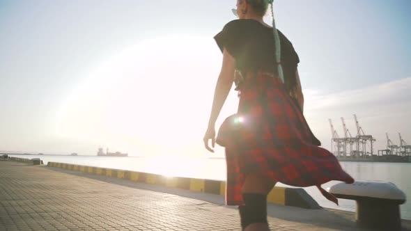 Young Stylish Funky Girl with Green Hair Riding Roller Skates and Dancing Near Sea Port During