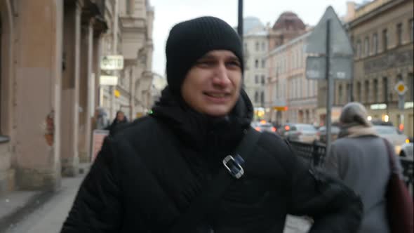 Serious Tired Man In Black Walks On The Street. Man Walking Down The City Street And Drinking Coffee