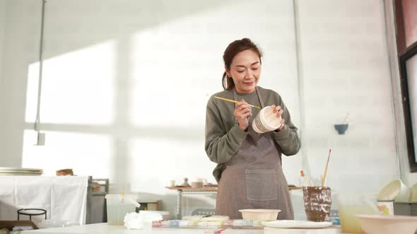 4K Asian woman enjoy painting self-made pottery mug at pottery workshop studio.