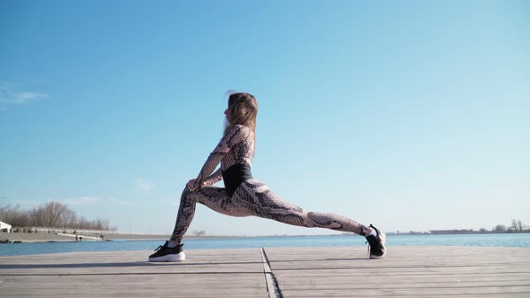 Woman Does Exercises on the Background of a Blue Lake. Doing Sports and Fitness Training Outdoor