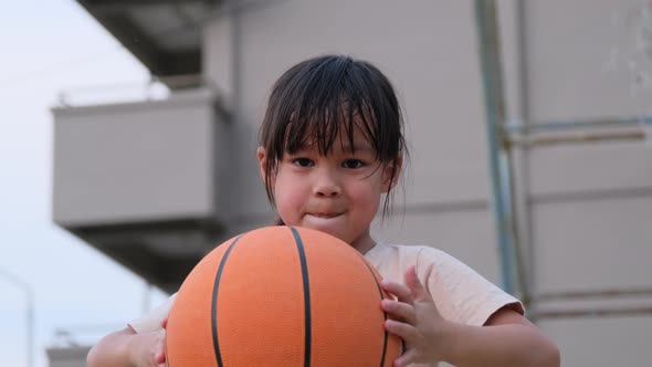 Cheerful cute girl holding basketball looking at camera at outdoor basketball playground.