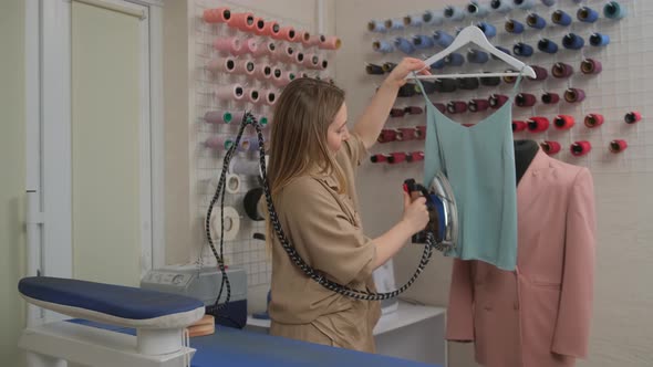 A fashion tailor designer at work hovering clothes with an iron and steam in a sewing workshop