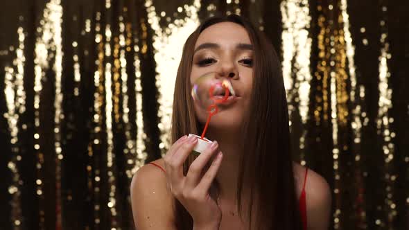 Party Fun. Woman Blowing Soap Bubbles On Shiny Golden Background