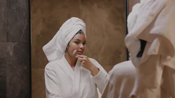 Young Darkskinned Brunette in Front of a Mirror in a Robe Massages Her Face