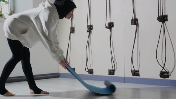 A Young Woman in Hijab Rolls Out the Yoga Mat on the Floor