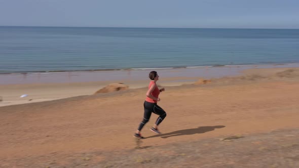 A Middleaged Woman Overweight Trains Cardio Jogging on the Beach for Weight Loss