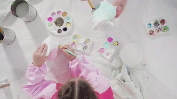 Flat lay. Little girl painting paper mache figurine at homeschooling art class.