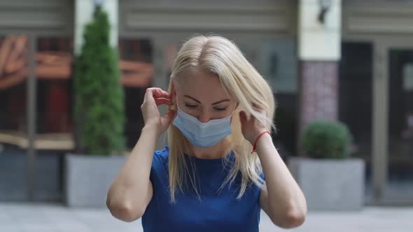 Portrait of a Charming Young Woman Looking Into the Camera and Putting on a Protective Medical Mask