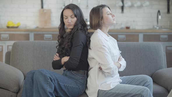 Argued Young Slim Women Sitting on Couch Back To Back with Crossed Hands