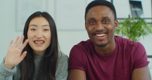 Close Up of Happy Multinational Couple Sitting on Sofa Calling on Webcam Video Chatting with Friends