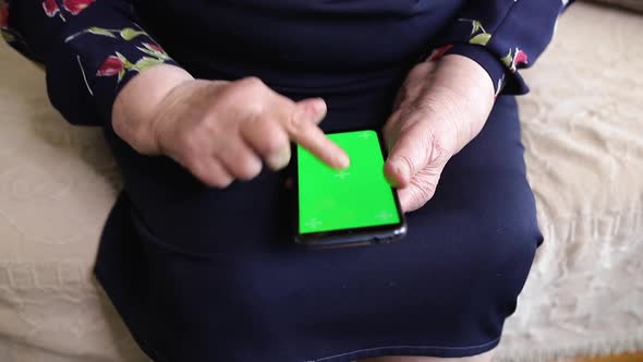 Phone with a green screen in the hands of an old woman