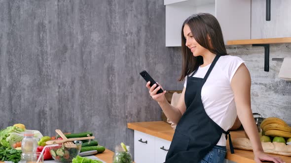 Smiling Housewife Chatting Using Smartphone Cooking Appetizing Healthy Food at Kitchen