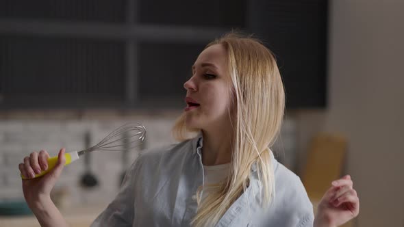 Happy Young Woman Dancing Singing While Cooking in Modern Kitchen