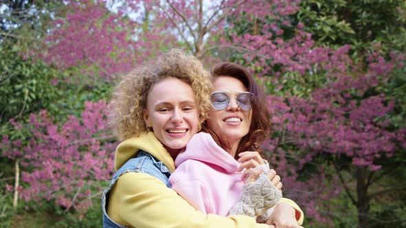 Homosexual Lesbian Couple Hugging in a Sakura Garden and Looks in To the Camera