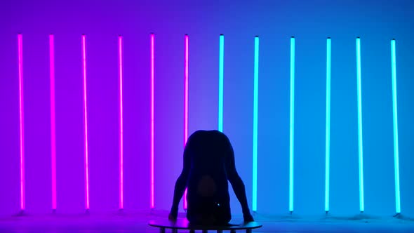 Silhouette of a Gymnast Against the Background of Pink and Blue Neon Lamps