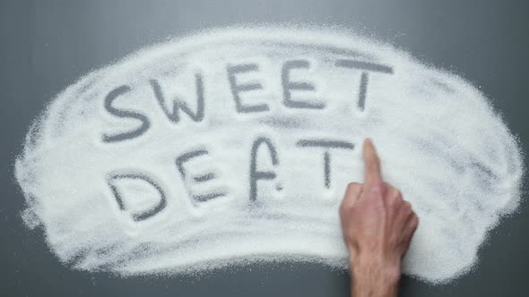 Hand writes words sweet death on sugar surface.