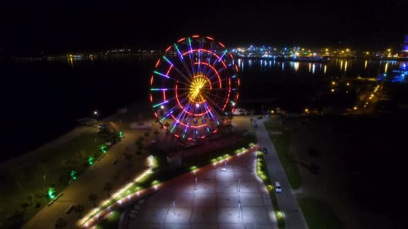 Ferris Wheel Sparking with Lights, Batumi Nightscape Reflecting in Black Sea