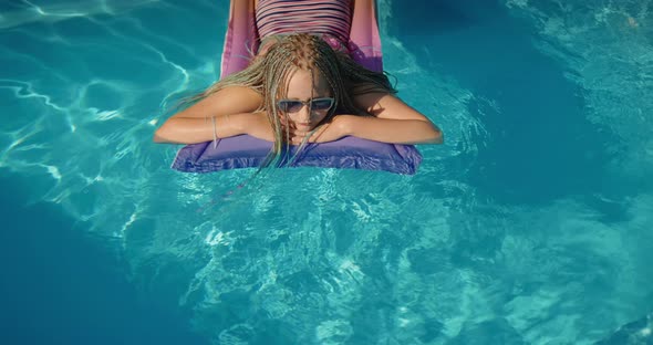 A Child with Afro Pigtails Swims on an Inflatable Mattress in the Pool Resting and Enjoying the Rest