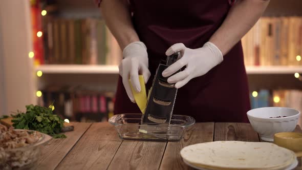 Closeup of Cooks Hands in Gloves Who is Grating Cheese Standing at a Wooden Table