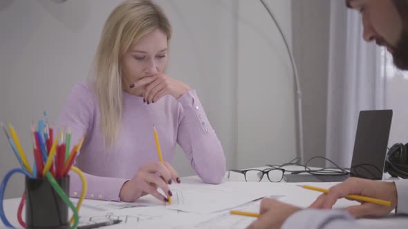 Thoughtful Caucasian Woman Listening To the Ideas of Her Male Colleague and Looking at Blueprints