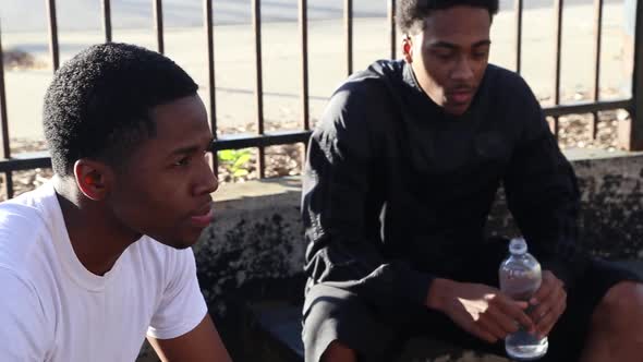 Two young basketball players drinking water while taking a break from playing.