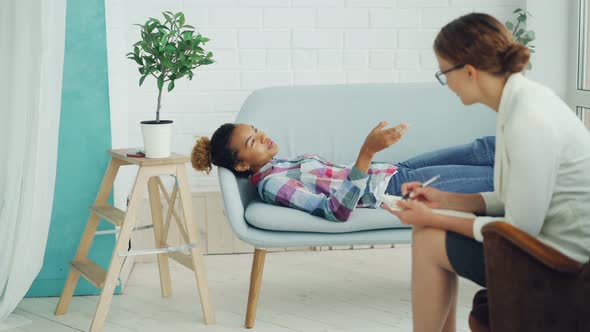 African American Teenager Is Talking To Psychologist Lying on Couch and Smiling