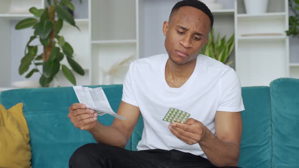 Black Man Alone Sitting on Sofa Sick Reading Instructions How To Take Pills Concentrated