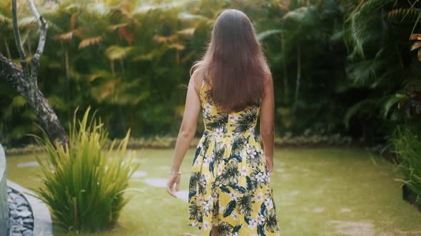 Woman Walks Through Tropical Garden to Camera Touches Hair with Hands Smiles