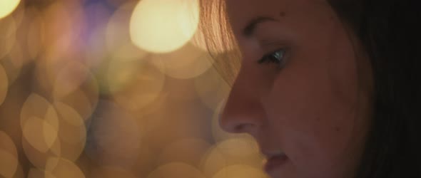 Close up of a young woman's face looking at her phone, night city bokeh lights