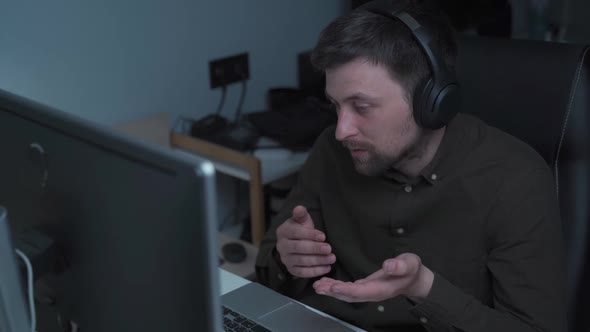 Focused Man Wearing Headphones Holding Video Call with Clients at Computer