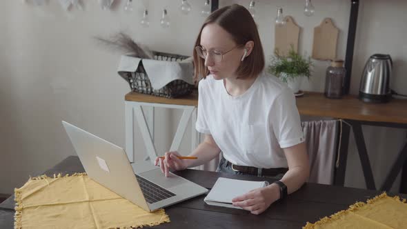 Close Up Serious Focused Woman with Ear Buds Looking at Laptop Screen Sitting at Desk Writing in