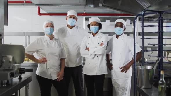 Portrait of diverse group of chefs wearing face masks standing in restaurant kitchen