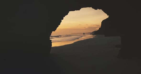 Slow Motion Sunlight Silhouette of Hole at Rocky Wall on Sand Ocean Coast