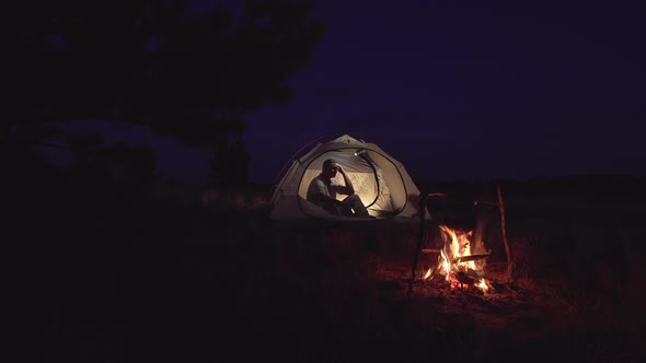 A Man Rests in a Tent Near a Fire