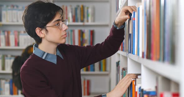 Young College Student Taking Book From Shelf in Library