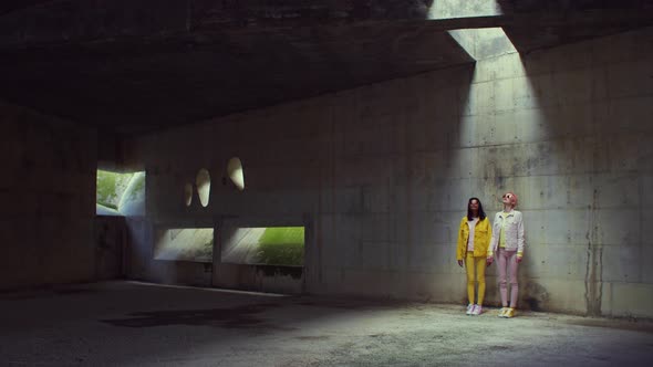 Two fashionable women standing inside of an abandoned building