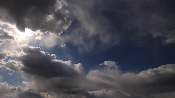 Beautiful 4K time lapse. Sun rays break through white fluffy clouds on vivid blue sky