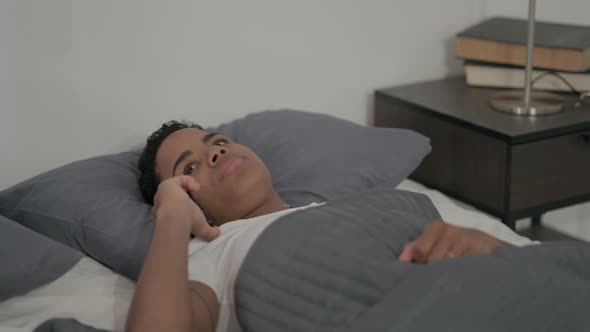 African Woman Talking on Smartphone While Sleeping in Bed
