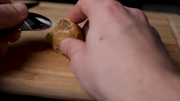 Using a spoon to scrap the skin from a ginger tuber.