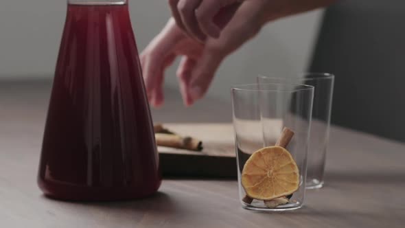 Slow Motion Man Hand Serving Mulled Wine in Thin Tumbler Glasses on Walnut Table