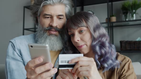 Mature Man and Young Woman Making Online Payment Using Smartphone and Credit Card at Home