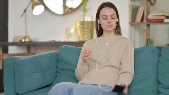 Young Woman Listening To Music on Smartphone on Sofa