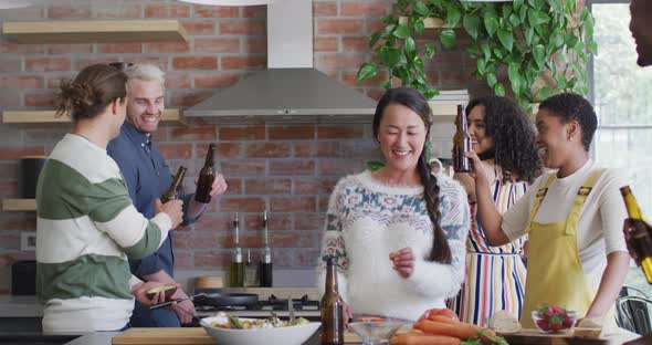 Happy group of diverse female and male friends with beer cooking together in kitchen