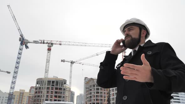 Businessman Talking on the Phone on the Background of the Construction Site