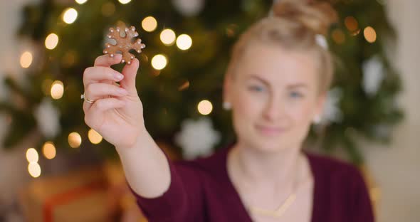 Woman Holding Snowflake Shape Cookie Against Christmas Tree