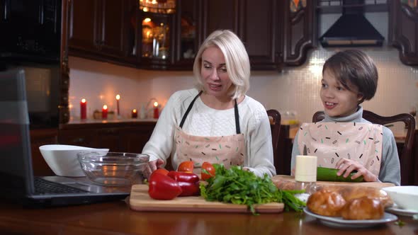 Cheerful Mother and Son Cooking Dinner and Talking on Laptop