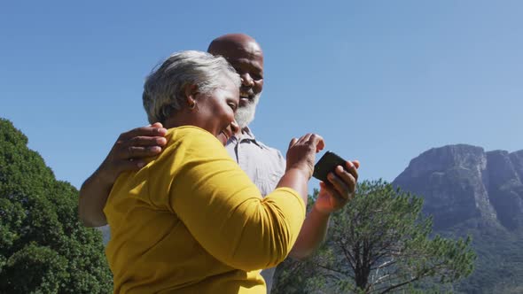 Happy senior african american couple using smartphone taking selfie in sunny garden